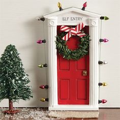 a red door with a christmas wreath on it next to a small tree and other decorations