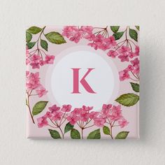 the letter k is surrounded by pink flowers and green leaves on a light pink background