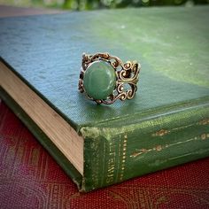 12x10mm green aventurine cabochon on an antiqued brass adjustable filigree ring. Easy to adjust to any size. Shade of green may vary slightly if at all. Also available in antiqued silver (as seen in the last photo). Matching earrings: https://www.etsy.com/listing/95714133/aventurine-and-brass-earrings About the stone: Medium green with a metallic iridescence caused by fuchsite (green mica) inclusions. Aventurine has been used in traditional cultures to promote leadership abilities. I do not reco Vintage Green Aventurine Jewelry, Adjustable Vintage Green Rings, Green Vintage Adjustable Rings, Adjustable Green Emerald Bohemian Ring, Adjustable Green Bohemian Emerald Ring, Adjustable Bohemian Green Emerald Ring, Vintage Adjustable Emerald Ring, Mha Genderbend, Earthy Rings