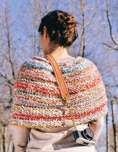 a woman wearing a multicolored knitted shawl with a camera in her hand