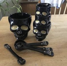 a wooden table topped with black skull cups and spoons