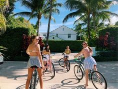 several girls riding bikes in front of some palm trees and houses on the other side