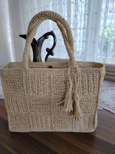 a woven bag sitting on top of a wooden table next to a vase and window