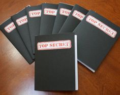 five black notebooks with top secret stickers on them sitting on a wooden table