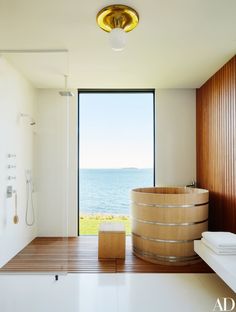 a bath room with a large window and a wooden tub in front of the ocean