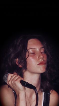 a woman with her eyes closed holding a microphone in front of her face and wearing a black strap around her neck