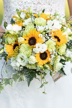 a bride holding a bouquet of sunflowers and greenery