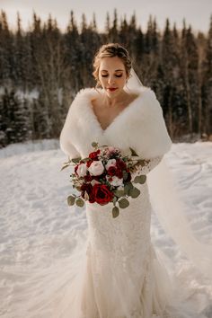 a woman in a wedding dress standing in the snow with her bouquet and fur stole around her neck