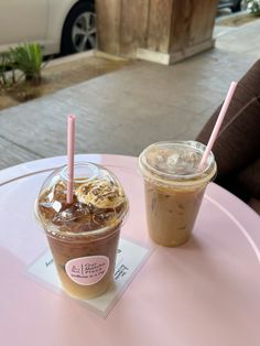 two iced coffees sitting on top of a pink table