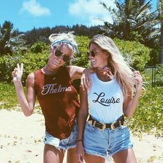 two young women standing next to each other on a sandy beach with trees in the background