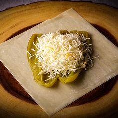 a green pepper covered in shredded cheese on top of a wooden plate with a napkin