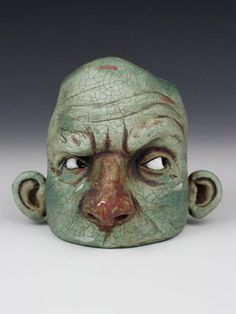 a green ceramic head with an odd look on it's face is shown in front of a gray background