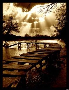 a wooden dock sitting on top of a river under a sky filled with lots of clouds