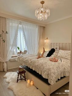 a woman laying on top of a bed in a bedroom next to a chandelier