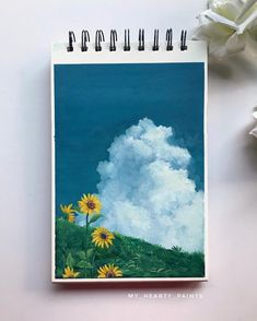 a spiral notebook with sunflowers and clouds in the background