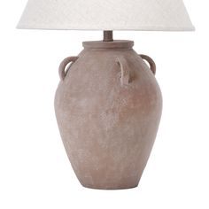 a light brown vase with a white shade on the top is sitting next to a lamp