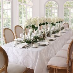 a dining room table is set with white flowers and place settings