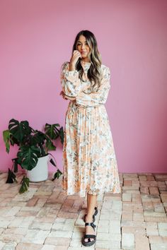 The Oakley Midi dress in a cream base with a peach and brown rose floral design is both stylish and functional. With a high neck, zipper in the back, and long sleeves with elastic cuffs, this dress is comfortable and easy to wear. The elastic waist with a tie creates a flattering silhouette, while the pleated bottom adds a touch of elegance. Model is wearing a small and is 5'8". Plus model is wearing a 2X and is 5'11". Size Chart Length Bust Waist S 47" 34" 32" M 47" 37" 34" L 47.5" 40" 36" XL 47.5" 44" 38" XXL 48" 48" 41" XXXL 48.5" 52" 44" *Measurements are approximate and are measured while hanging* Fabric and Care 100% Polyester Hand wash cold. Do not bleach. Lay flat to dry. Low iron if needed or dry clean. Tiered Dresses, Plus Model, Teen Dress, Hanging Fabric, Cream Base, Spring Fits, White Outfits, Floral Maxi Dress, Jeans Dress