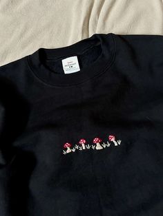 This hand embroidered black mushroom toadstool crewneck sweatshirt is a perfect simple capsule piece that will keep you cozy this fall! Unisex sizing and preshrunk cotton material, making it super comfortable and easy to wear.  CARE:  -Turn inside out, and wash cold on delicate -Hang dry -Turn inside out to iron Each Sweater is hand embroidered and by nature may vary slightly from the I,age shown. Each embroidered piece is my own original design. We use Hanes EcoSmart sweatshirts for this design, using recycled plastic bottles to create soft yarns for their sweatshirts! This piece cannot be customized. If you would like a customized sweatshirt, please message me! Keep up to date by Facebook and Instagram accounts at @MistyMountainsCo Embroidered Mushrooms Simple, Embroidery Mushrooms, Forest Embroidery, Embroidered Sweaters, Black Mushroom, Patchwork Clothes, Fall Forest, Black Crewneck Sweatshirt, Embroidery Shirt