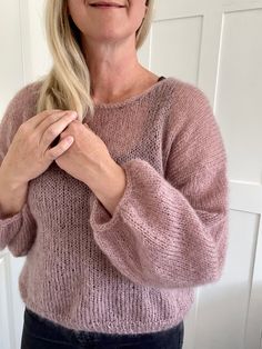 a woman wearing a pink sweater standing in front of a door with her hands on her chest