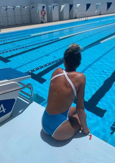 a woman sitting on the edge of a swimming pool next to an empty pool with no people