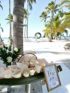 a table that has some cups on it and flowers in front of palm trees at the beach