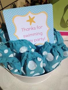 a bowl filled with blue and white polka dot cloths next to a sign that says thanks for swimming my party