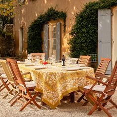 an outdoor dining table with chairs and a yellow table cloth on it in front of a house