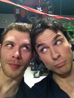 two men posing for the camera in front of a red ribbon