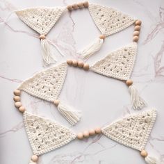 a white crocheted triangle with wooden beads and tassels on a marble surface