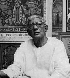 black and white photograph of an old man sitting in front of some art on the wall