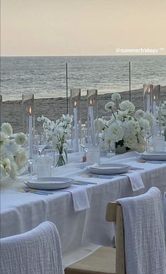 a table set up with white flowers and candles on the beach side for an event