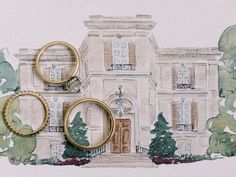 two gold wedding rings sitting on top of each other in front of a large building