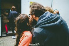 a man and woman kissing each other in front of a building with people standing around