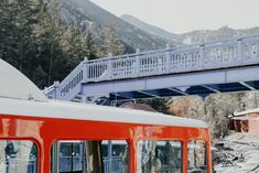 an orange and white train traveling under a bridge