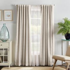 a living room with white curtains and a chair in front of a window that has a potted plant on top of it