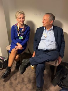 an older man and woman sitting next to each other in a room with luggage on the floor