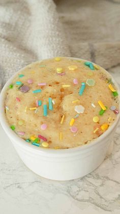 a cake in a white bowl with sprinkles on the table next to it