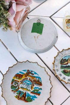 three plates with different designs on them sitting on a tile floor next to pink flowers