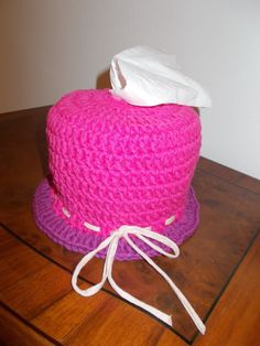 a crocheted hat with a tissue paper on it sitting on a wooden table