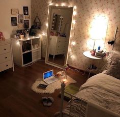 a bedroom with lights on the wall and a laptop computer sitting on the floor in front of a mirror