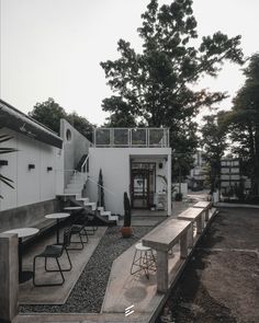 an outdoor dining area with tables and stools in front of a white building surrounded by trees