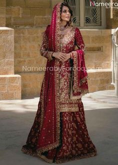 a woman in a red and gold bridal gown standing outside with her hands on her hips