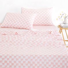 a pink and white checkered comforter set with pillows on a wooden side table