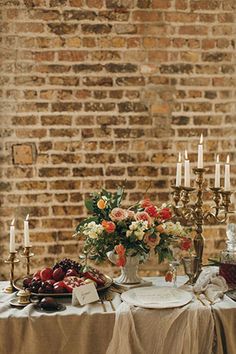 the table is set with candles, fruit and flowers in front of a brick wall