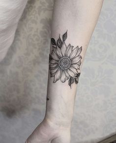 a woman's arm with a black and white sunflower tattoo on the wrist