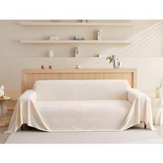 a couch covered in a white blanket next to a table and shelves with vases