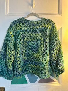 a green crocheted sweater hanging on a white door