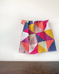 a multicolored quilt hanging on a clothes line in front of a white wall