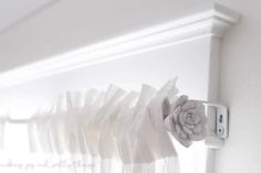 the curtain is hanging on the wall and there are white curtains with flowers attached to them